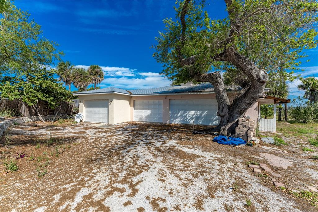 A single-story house with a three-car garage and a large tree in the front yard — 6039 MANASOTA KEY ROAD, ENGLEWOOD, FL