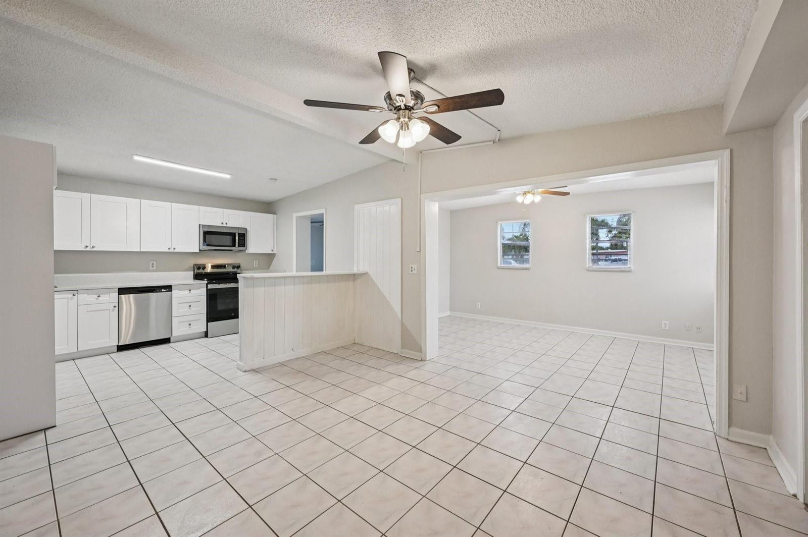 A kitchen with white cabinets and stainless steel appliances opens into a tiled living area — 5618 Cinnamon Drive, West Palm Beach FL 33415, WEST PALM BEACH, FL