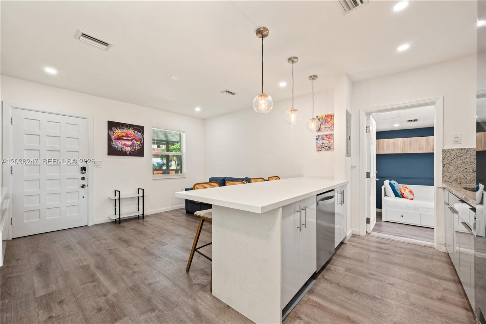 A modern kitchen features a white island with bar seating, pendant lights, and wood flooring — 329 SW 15th Ave, Miami FL 33135, MIAMI, FL