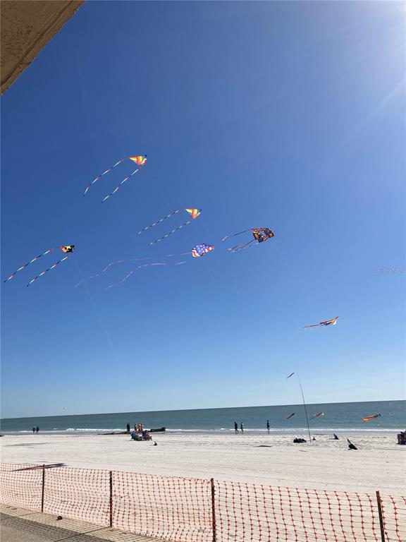 Several colorful kites fly over a sandy beach under a clear blue sky — 14900 GULF BOULEVARD UNIT 113, MADEIRA BEACH, FL