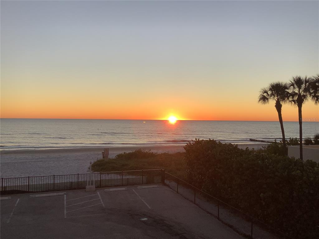 A parking lot sits in front of a beach with palm trees at sunset — 14900 GULF BOULEVARD UNIT 113, MADEIRA BEACH, FL