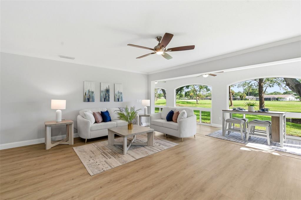 A bright living room features light wood flooring, two white sofas, and large arched windows — 5475 CHANTECLAIRE UNIT 58, SARASOTA, FL