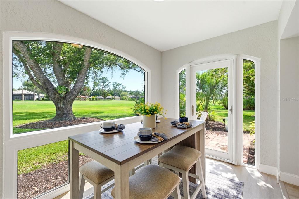 A sunroom features a dining table, large arched windows, and a glass door overlooking greenery — 5475 CHANTECLAIRE UNIT 58, SARASOTA, FL