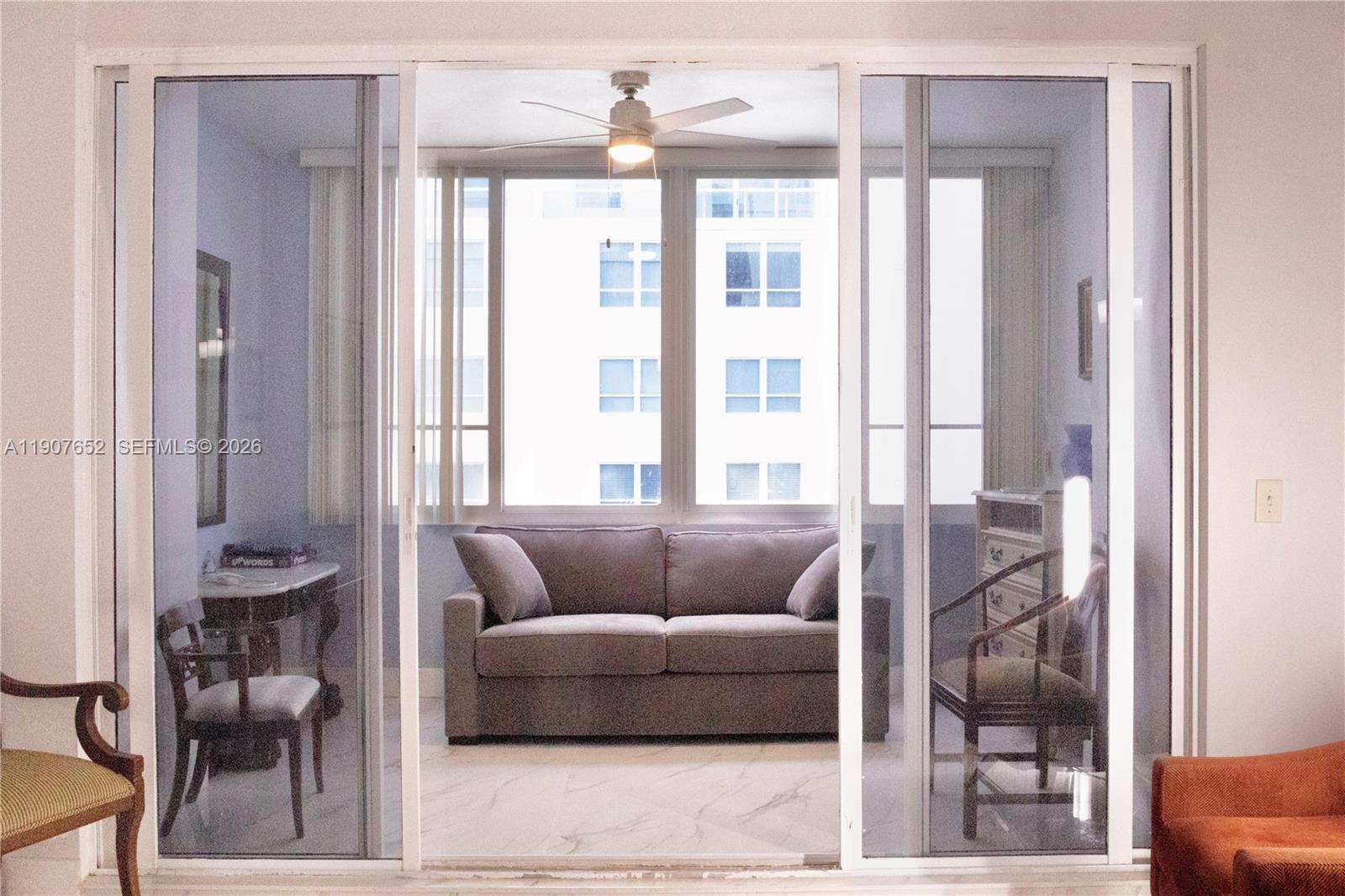 A sunroom with a sofa, ceiling fan, and tile flooring is viewed through sliding glass doors — 5005 Collins Ave # 1523, Miami Beach FL 33140, MIAMI BEACH, FL