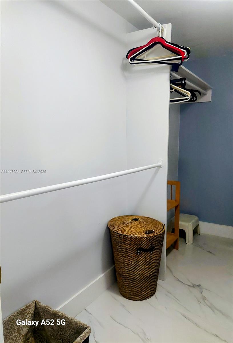 A closet features white walls, a hanging rod, a wicker hamper, and marble-look flooring — 5005 Collins Ave # 1523, Miami Beach FL 33140, MIAMI BEACH, FL