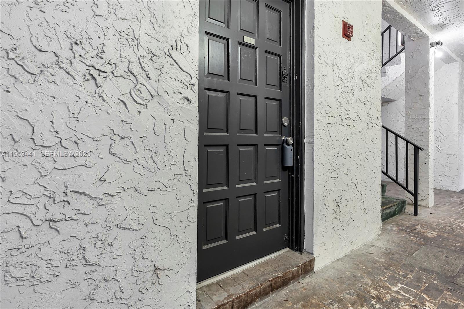 A dark-colored door with a lockbox is set into a textured white stucco wall — 3300 Spanish Moss Ter # 106, Lauderhill FL 33319, LAUDERHILL, FL