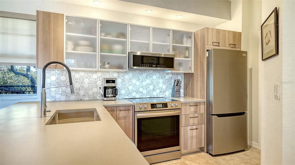 A modern kitchen features light wood cabinets, stainless steel appliances, and a hexagonal tile backsplash — 1268 11TH STREET UNIT 2403, SARASOTA, FL