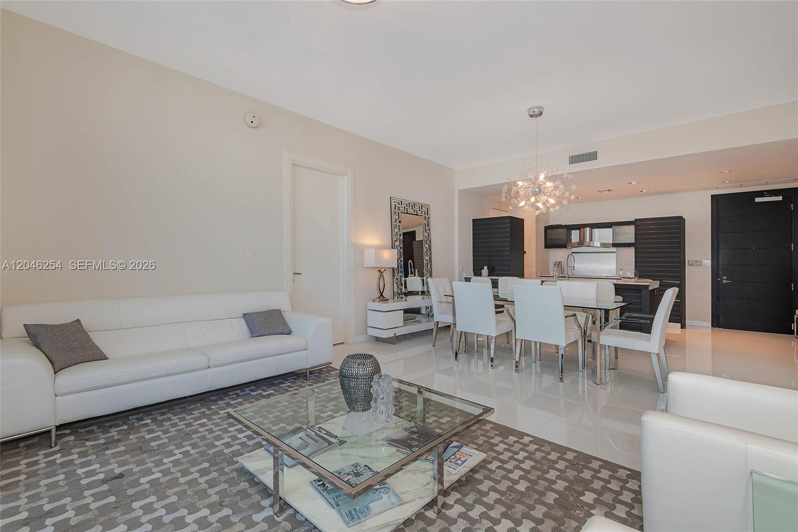 A modern living and dining area features white tile floors, a white sofa, and kitchen — 200 Biscayne Boulevard Way # 5109, Miami FL 33131, MIAMI, FL