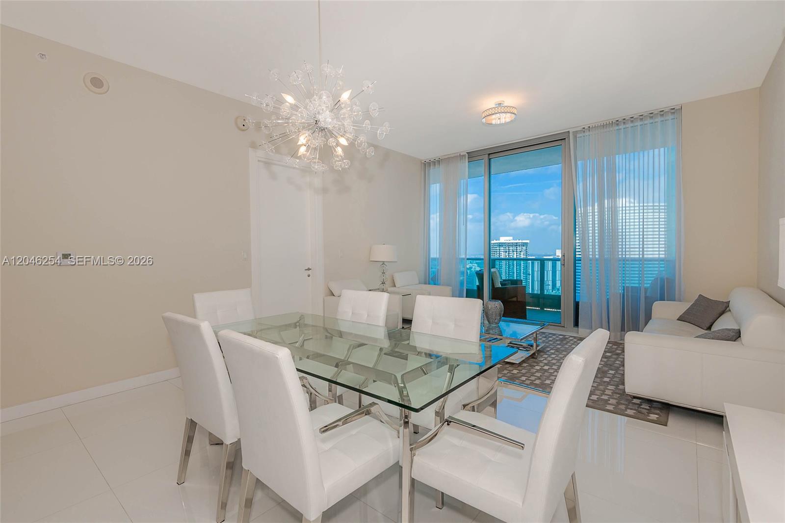 A dining area with a glass table and white chairs overlooks a balcony with views — 200 Biscayne Boulevard Way # 5109, Miami FL 33131, MIAMI, FL