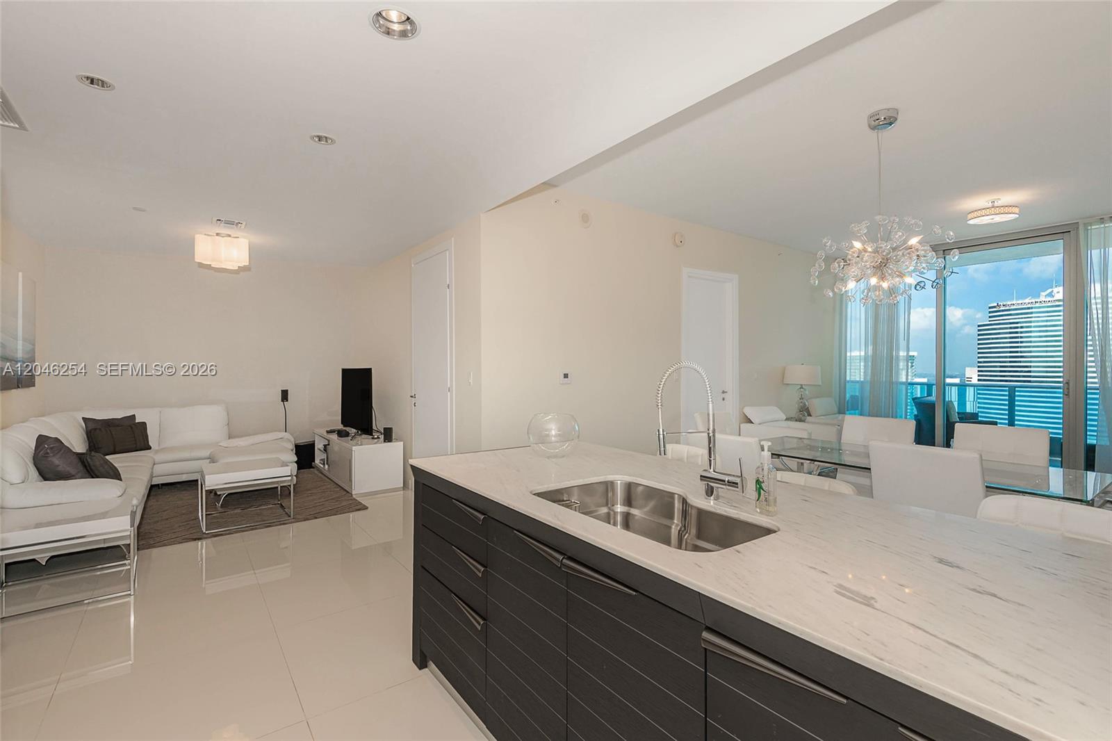 A modern kitchen island with a sink overlooks an open-concept living and dining area — 200 Biscayne Boulevard Way # 5109, Miami FL 33131, MIAMI, FL