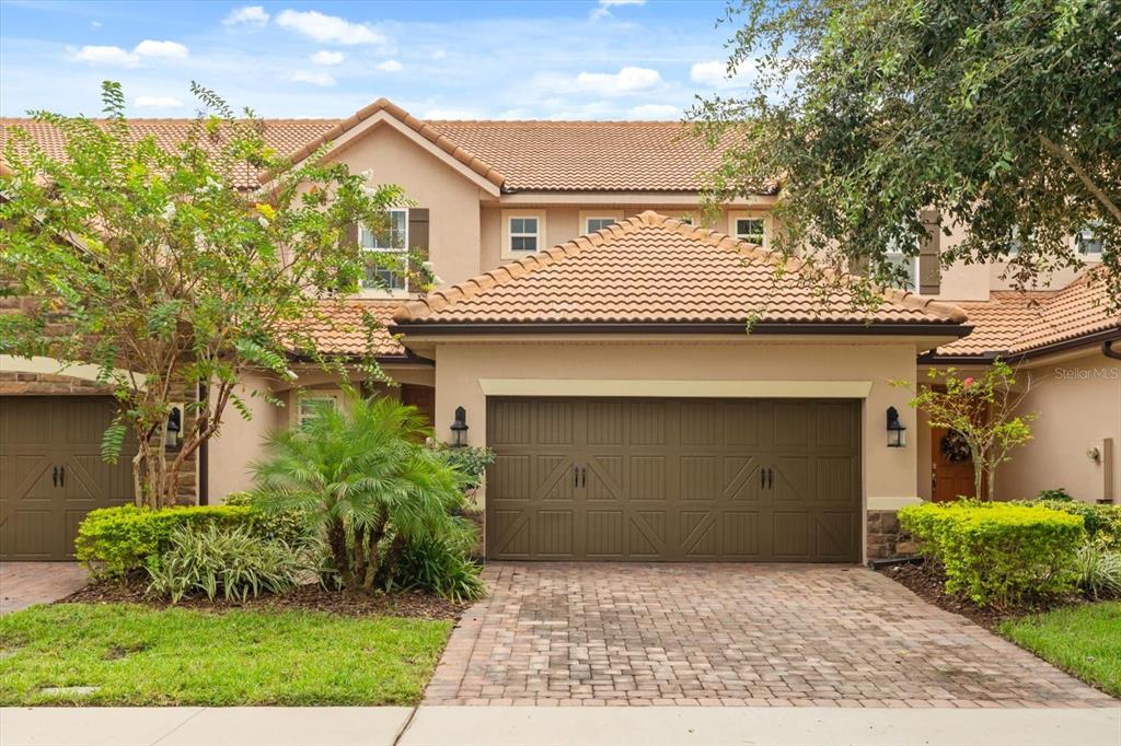 A two-story townhouse with a brown garage door, tile roof, and a brick paver driveway — 10613 BELFRY CIRCLE, ORLANDO, FL