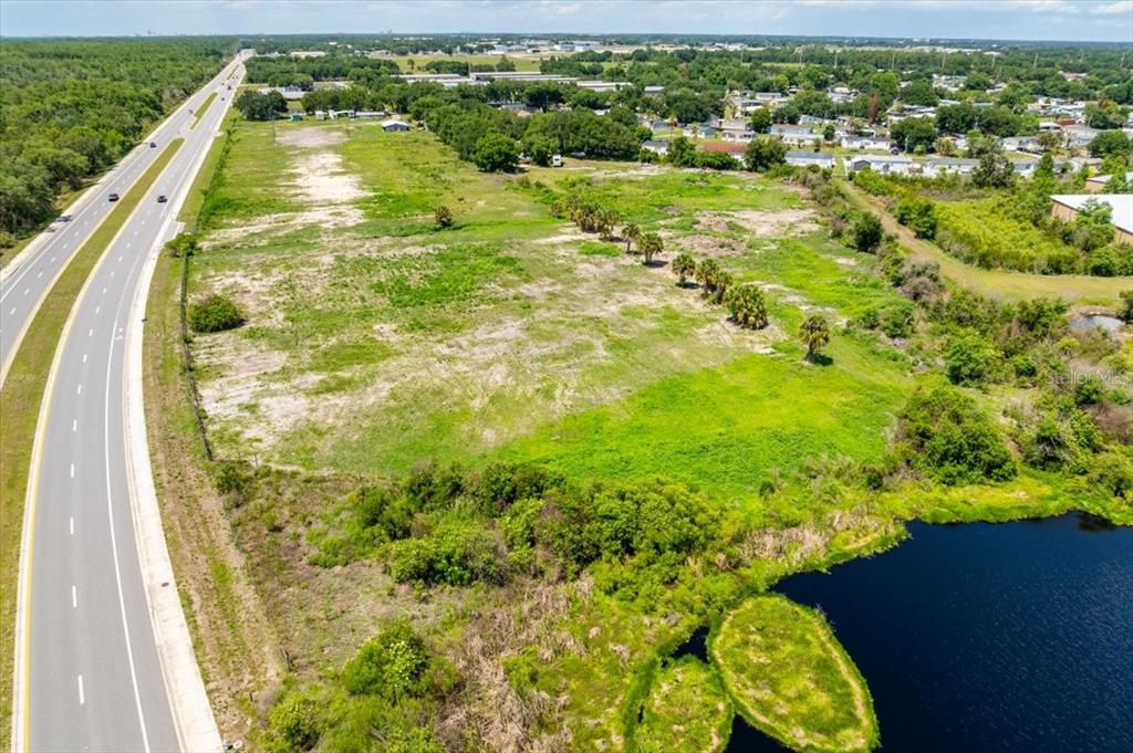 An aerial view shows a vacant grassy lot adjacent to a highway and a pond — 4043 DANA KATHERINE DRIVE, KISSIMMEE, FL