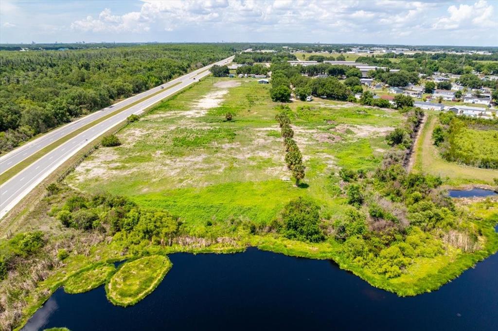 An aerial view shows a large, grassy vacant lot bordering a highway and a pond — 4043 DANA KATHERINE DRIVE, KISSIMMEE, FL
