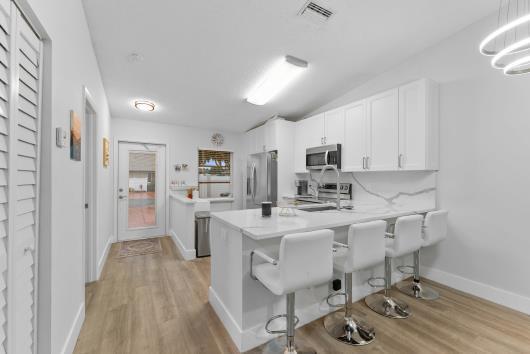 A modern kitchen with white cabinets and stainless steel appliances opens into a living area — 18861 Argosy Drive, Boca Raton FL 33496, BOCA RATON, FL