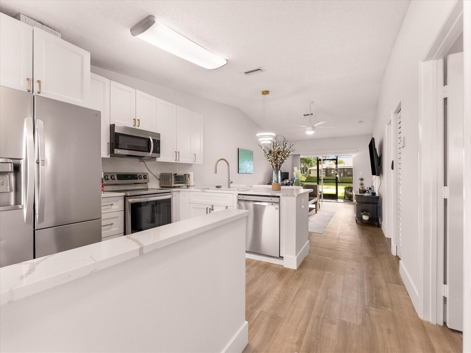 A modern kitchen features white cabinetry, a marble-topped breakfast bar with stools, and light flooring — 18861 Argosy Drive, Boca Raton FL 33496, BOCA RATON, FL