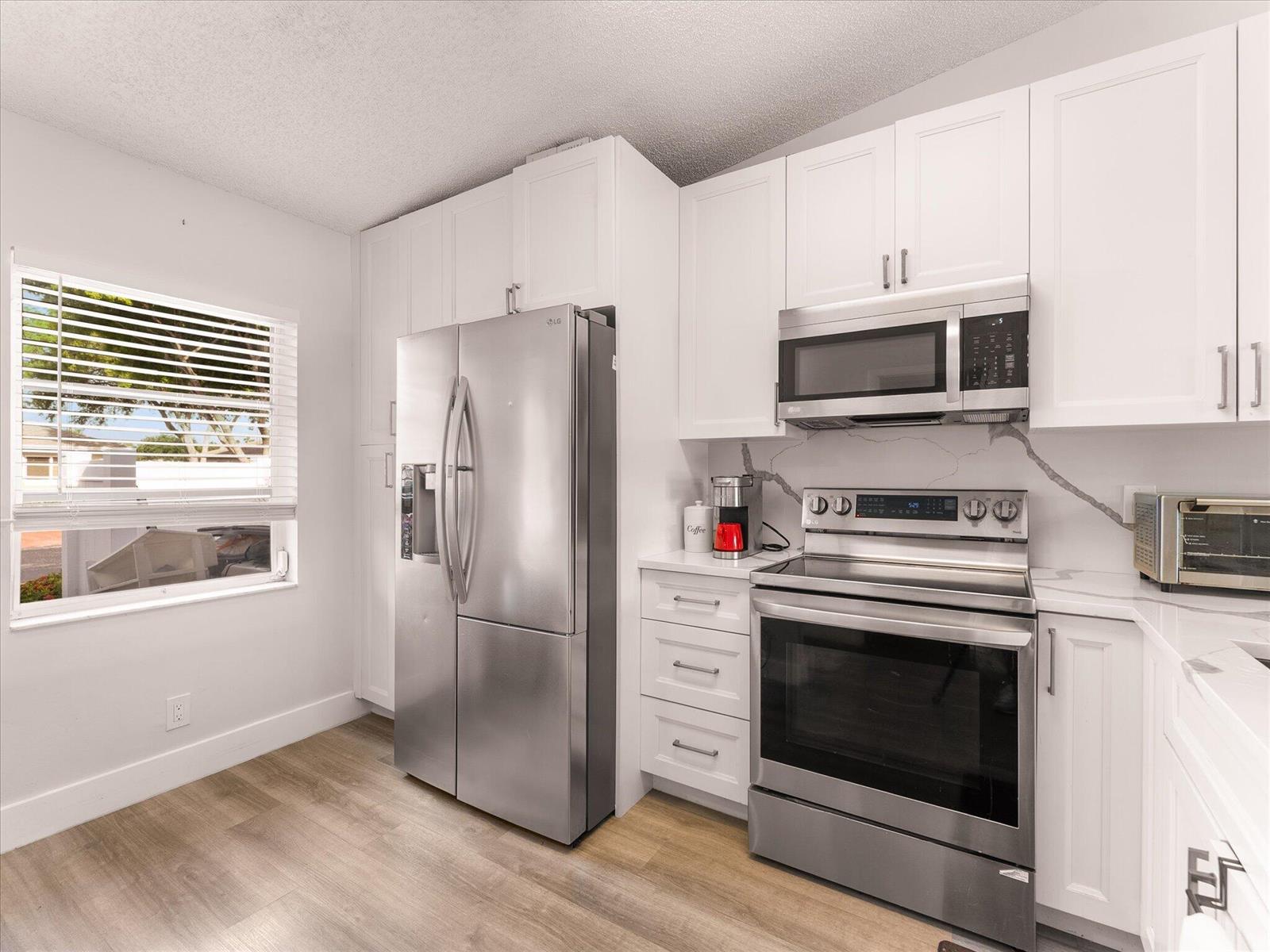 A kitchen features white cabinets, stainless steel appliances, a marble-look backsplash, and wood-look flooring — 18861 Argosy Drive, Boca Raton FL 33496, BOCA RATON, FL