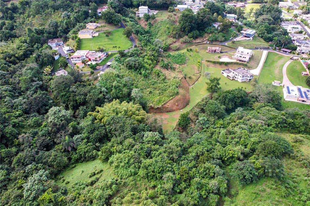 An aerial view shows houses scattered across a hilly, lush green landscape with paved roads — PR 568 KM 28.5 SECTOR EL LIMON PADILLA, COROZAL, PR