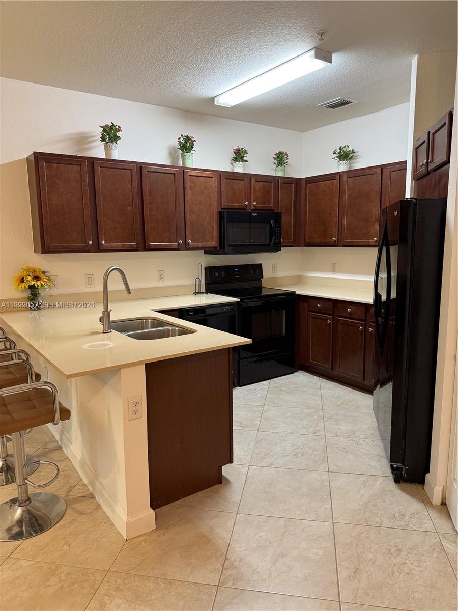 A kitchen features dark wood cabinets, black appliances, light countertops, and tile flooring — 290 NW 109th Ave # 107, Miami FL 33172, MIAMI, FL