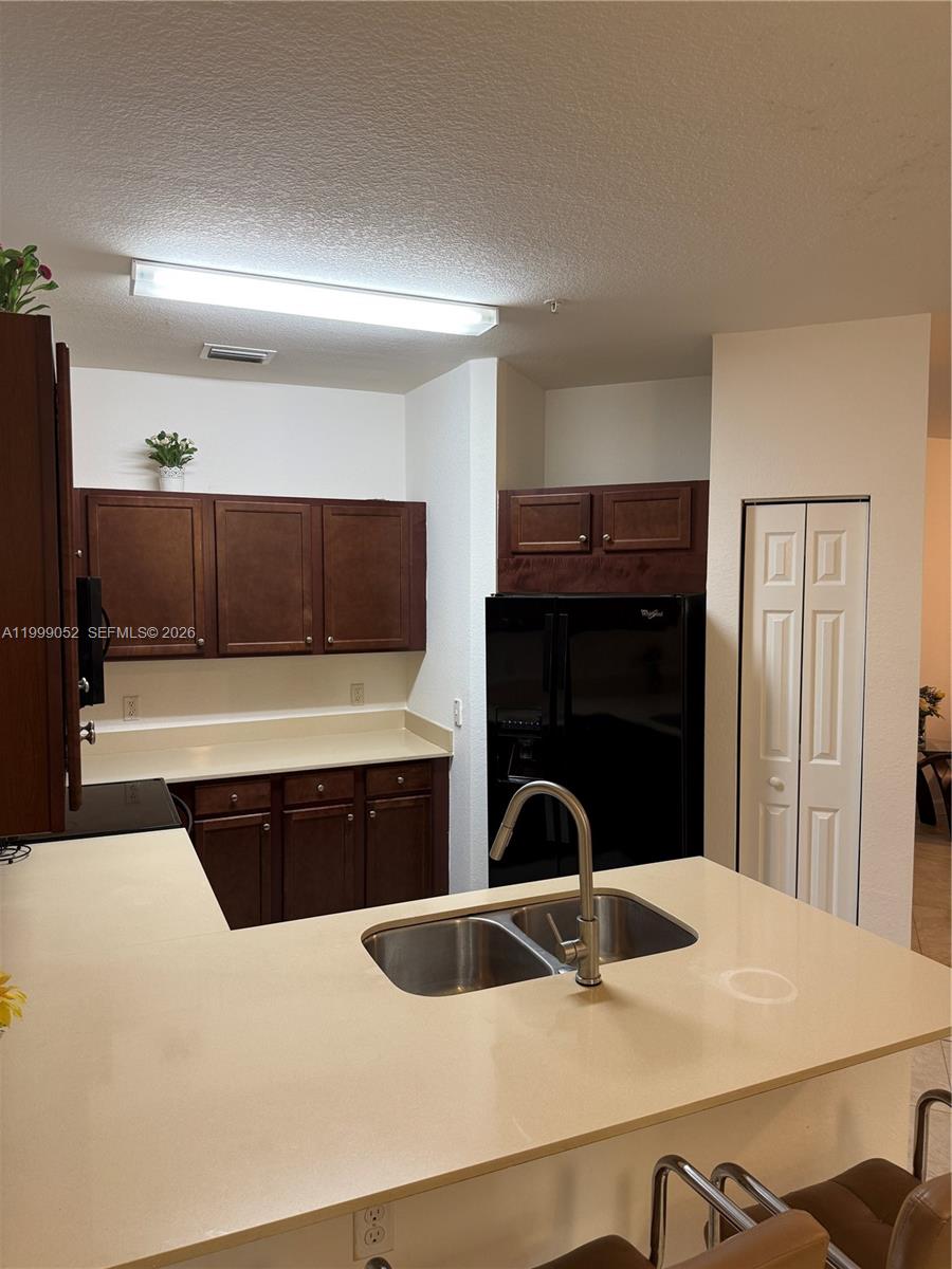 A kitchen features dark wood cabinets, beige countertops, a black refrigerator, and a sink island — 290 NW 109th Ave # 107, Miami FL 33172, MIAMI, FL
