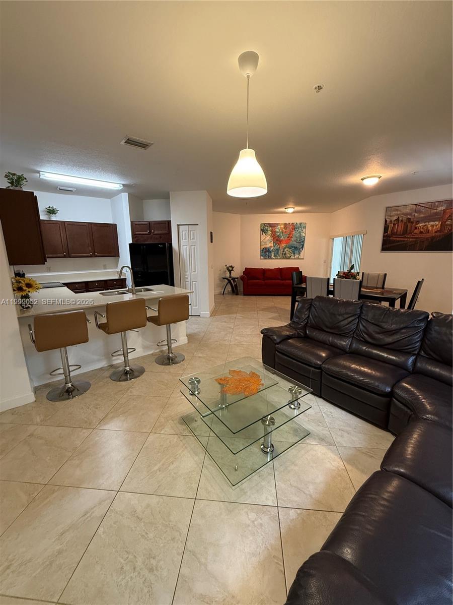 An open-concept living area features a kitchen with bar seating, tile floors, and a sectional — 290 NW 109th Ave # 107, Miami FL 33172, MIAMI, FL