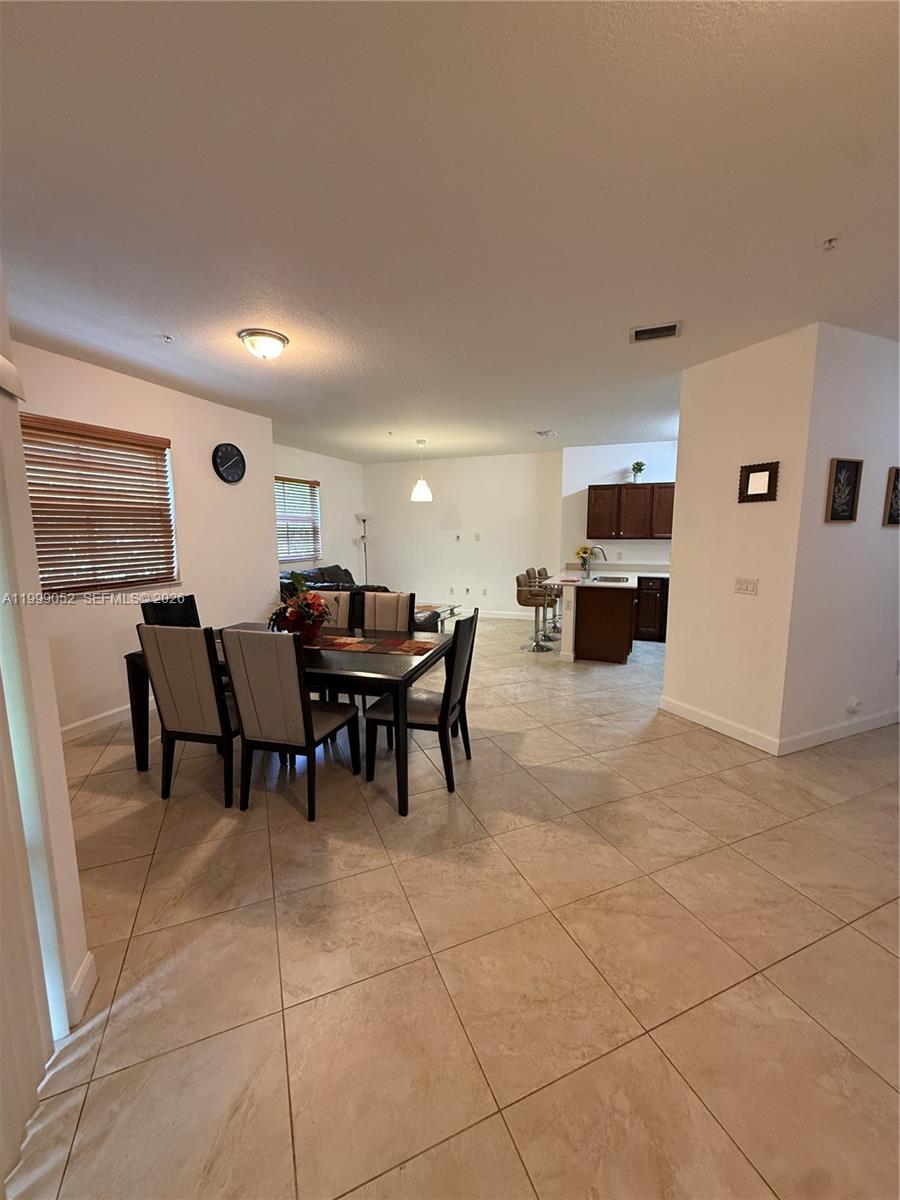 A dining area with a dark wood table and chairs sits adjacent to an open kitchen — 290 NW 109th Ave # 107, Miami FL 33172, MIAMI, FL