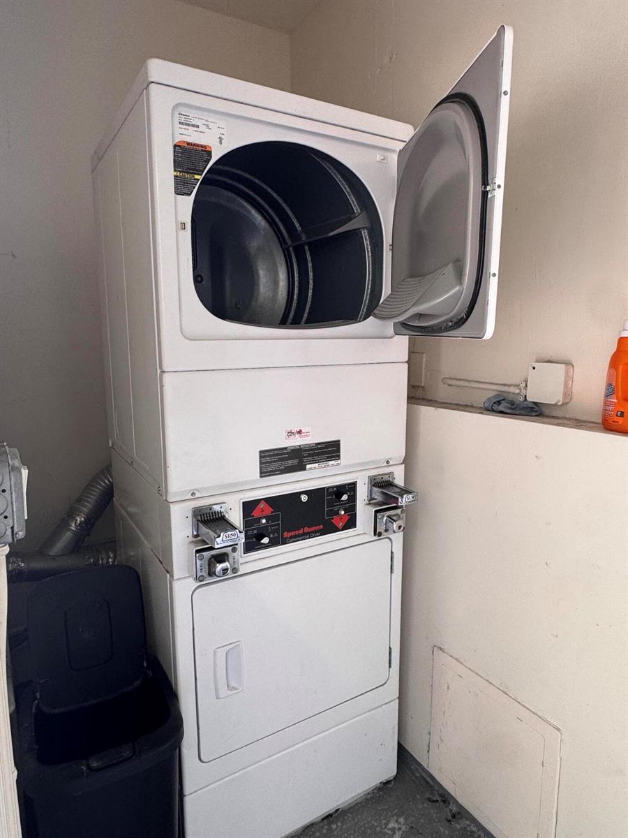 A white stacked coin-operated commercial dryer stands in a utility room — 570 NE 64th Street Unit 2, Miami FL 33138, MIAMI, FL
