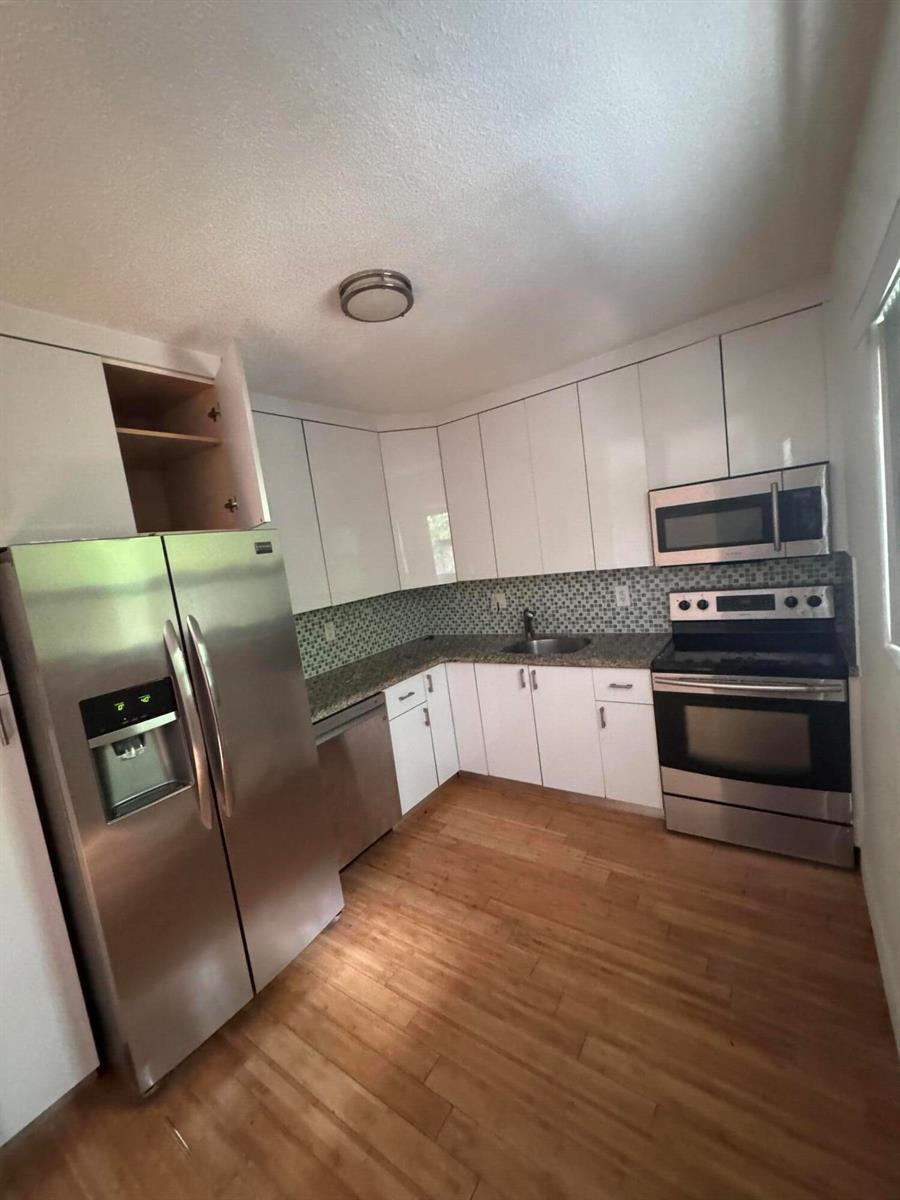 A kitchen features white cabinets, stainless steel appliances, a mosaic backsplash, and wood flooring — 570 NE 64th Street Unit 2, Miami FL 33138, MIAMI, FL