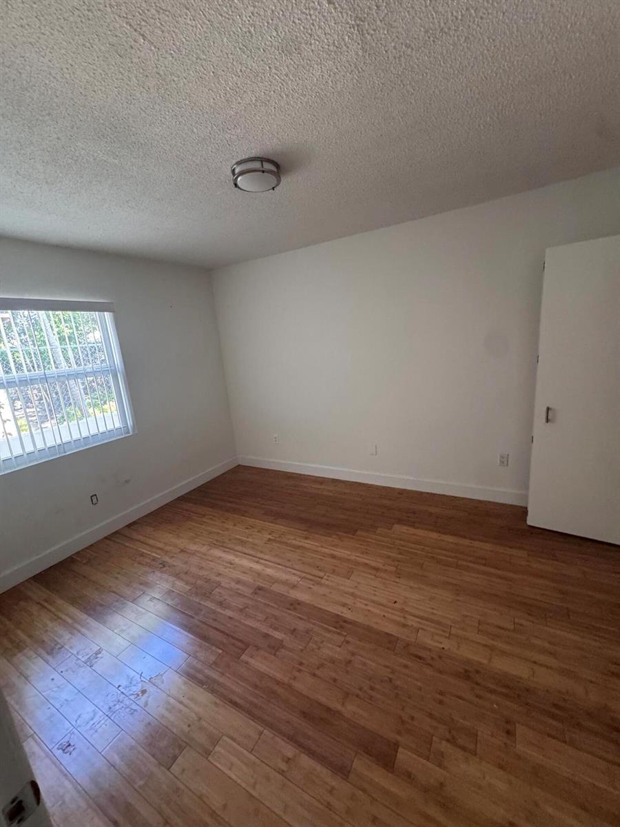 An empty bedroom features light-colored wood flooring, white walls, a window with blinds, and a closet — 570 NE 64th Street Unit 2, Miami FL 33138, MIAMI, FL