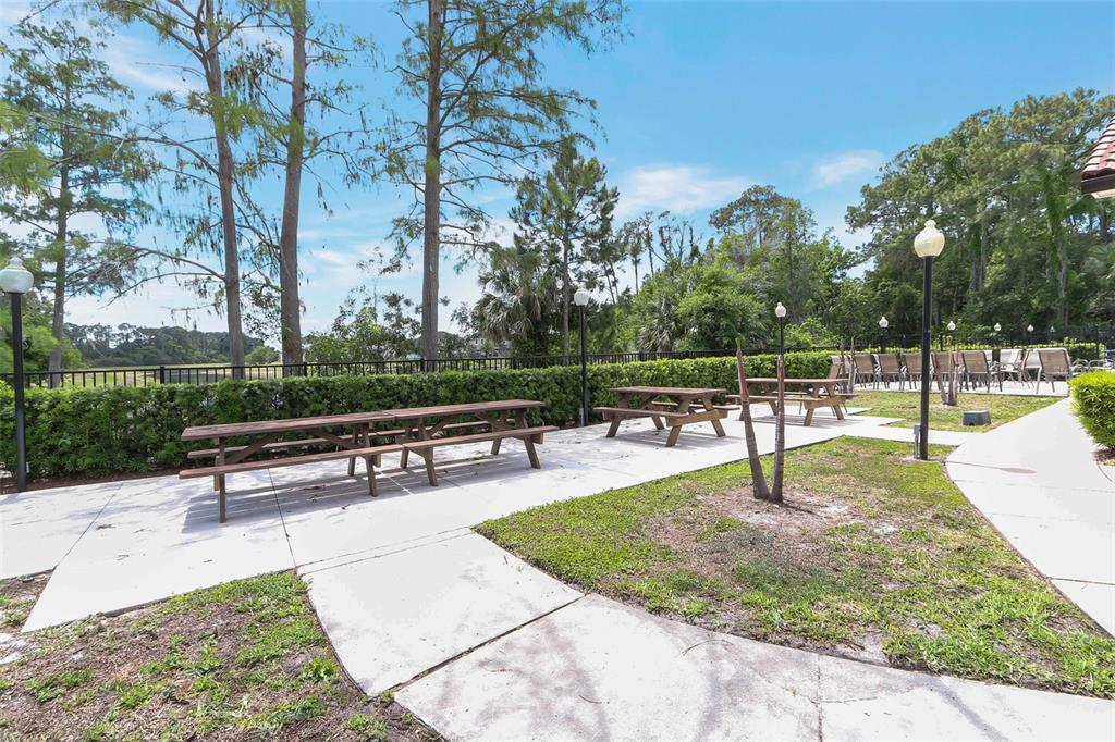 A paved outdoor patio features two wooden picnic tables and lamp posts near a hedge — 5160 CONROY ROAD UNIT 21, ORLANDO, FL