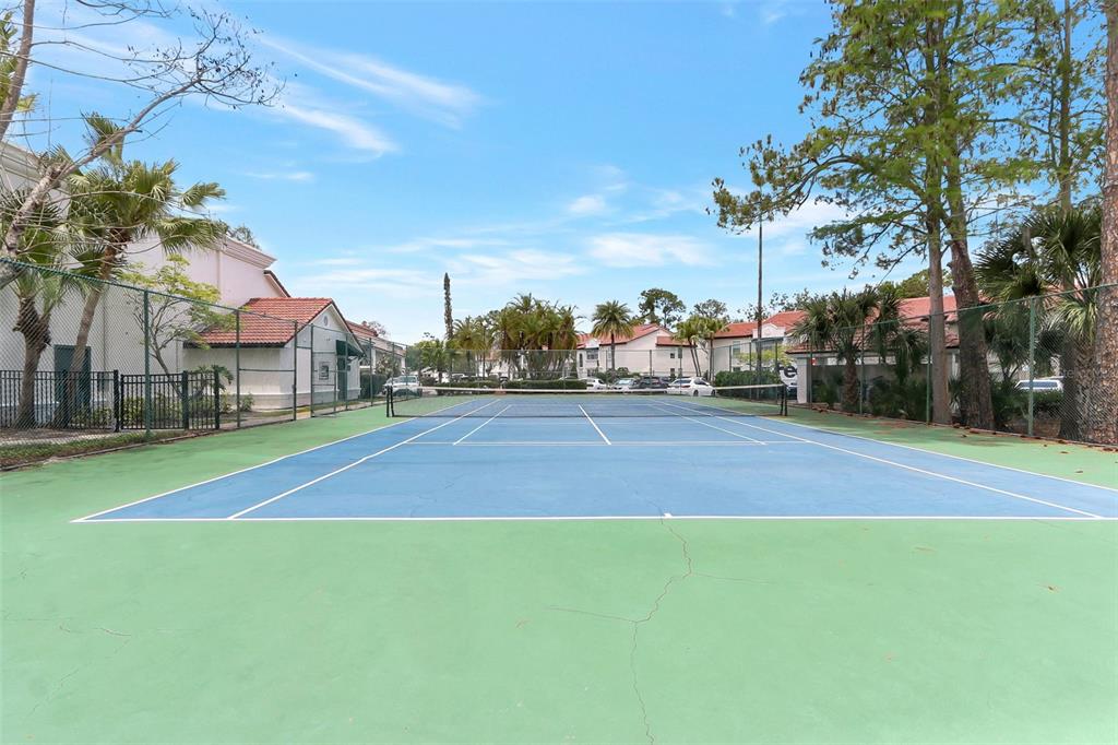 A fenced outdoor tennis court with a blue and green surface sits between residential buildings — 5160 CONROY ROAD UNIT 21, ORLANDO, FL