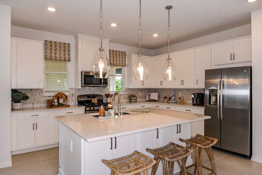 A modern kitchen features white cabinetry, a large island with bar seating, and stainless appliances — 14784 FIELD DAISY DRIVE, WINTER GARDEN, FL