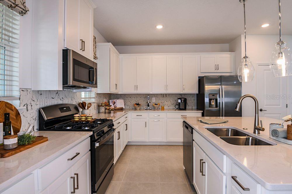 A modern kitchen features white cabinets, stainless steel appliances, a kitchen island, and quartz countertops — 14784 FIELD DAISY DRIVE, WINTER GARDEN, FL