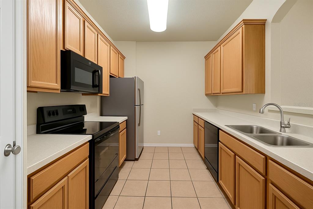 A galley kitchen features light wood cabinets, black appliances, white countertops, and beige tile flooring — 3326 ROBERT TRENT JONES DRIVE UNIT 10402, ORLANDO, FL