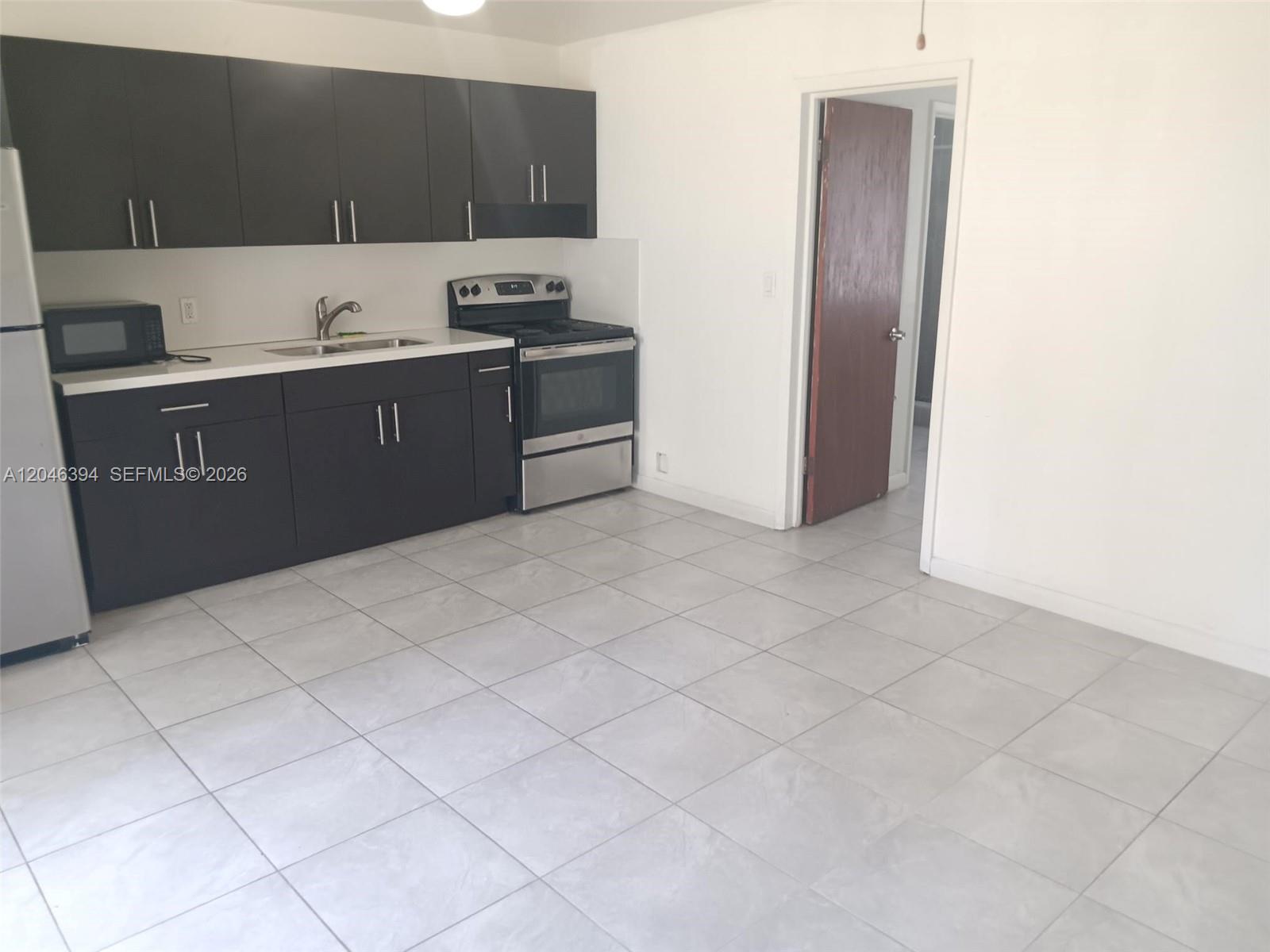 A kitchen features dark cabinets, stainless steel appliances, white countertops, and light-colored tile flooring — HOLLYWOOD, FL