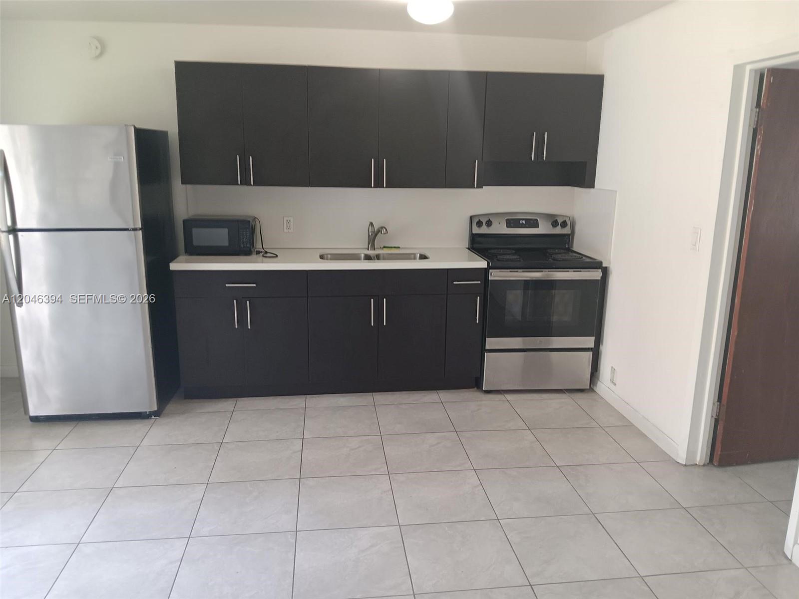 A kitchen features dark cabinets, stainless steel appliances, a white countertop, and light tile flooring — HOLLYWOOD, FL
