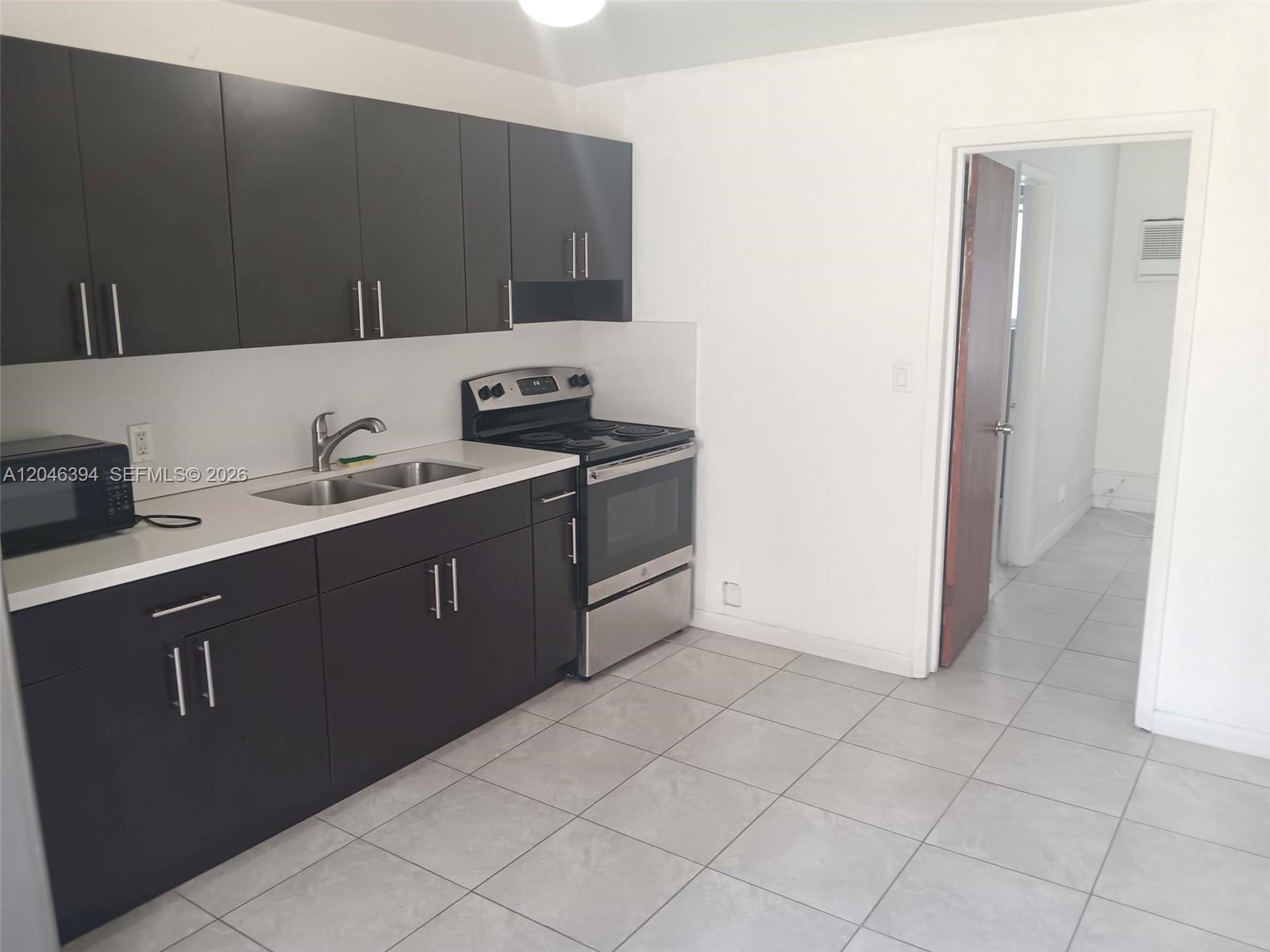 A kitchen features dark cabinets, stainless steel appliances, white countertops, and light tile flooring — HOLLYWOOD, FL