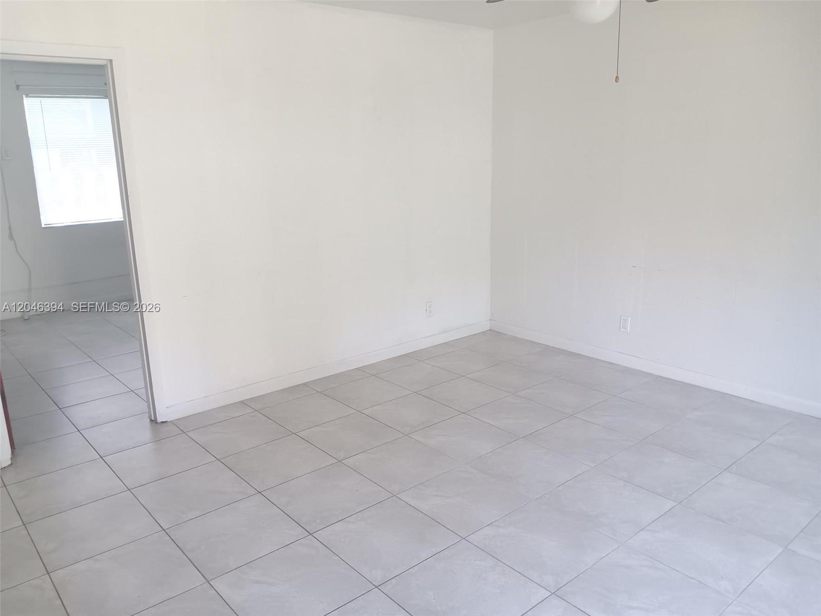 A room with white walls and light gray tiled flooring leads to an adjacent room — HOLLYWOOD, FL