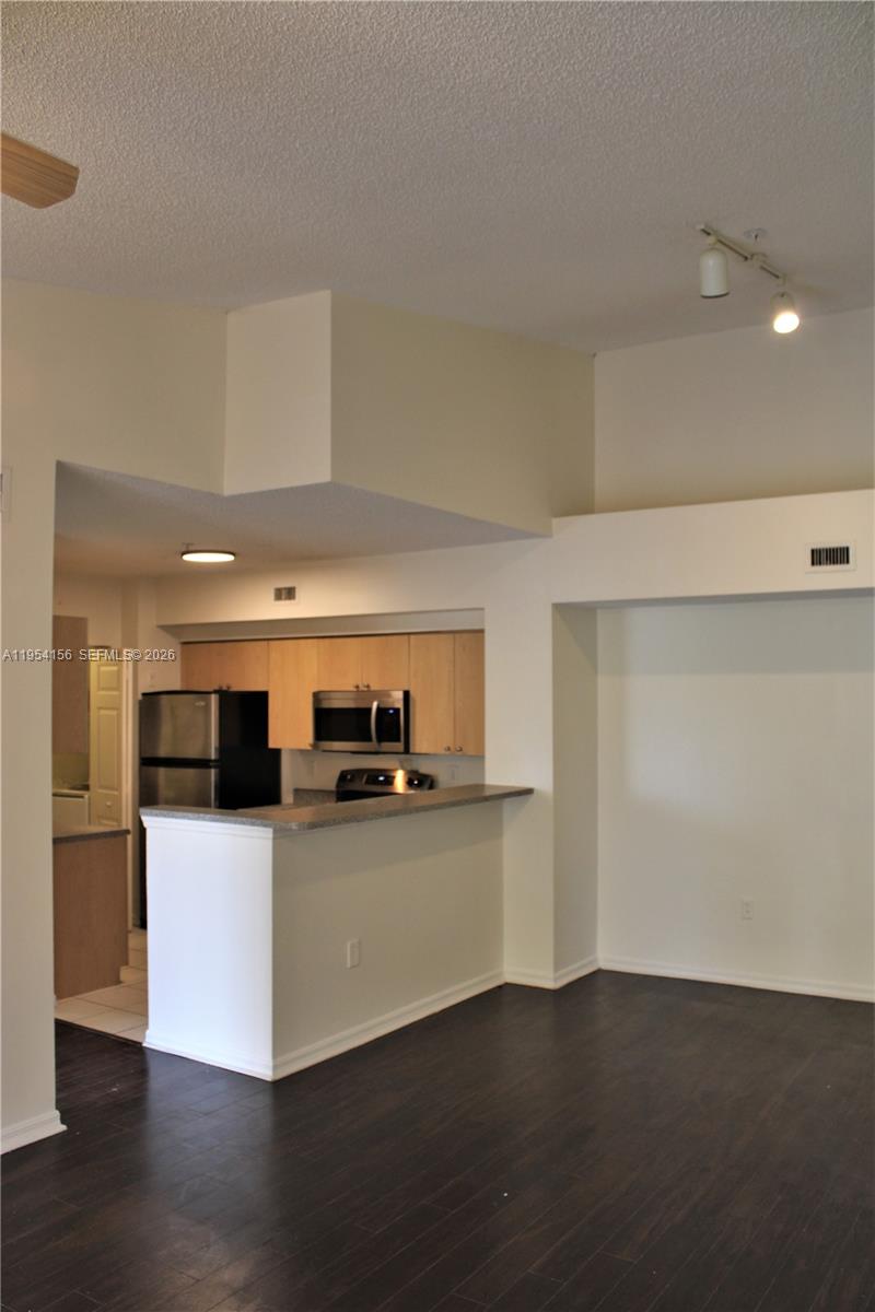 A kitchen with light wood cabinets and a breakfast bar overlooks a dark-floored living area — 2400 E Preserve Way # 304, Miramar FL 33025, MIRAMAR, FL