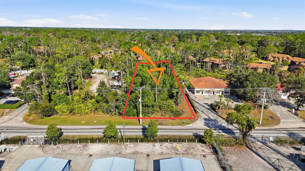 An aerial view shows a vacant, wooded lot outlined in red next to a commercial building — 19 UTILITY DRIVE, PALM COAST, FL