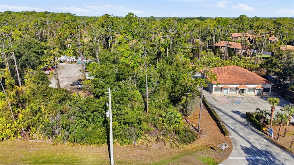 An aerial view shows a wooded lot adjacent to a commercial building and parking area — 19 UTILITY DRIVE, PALM COAST, FL