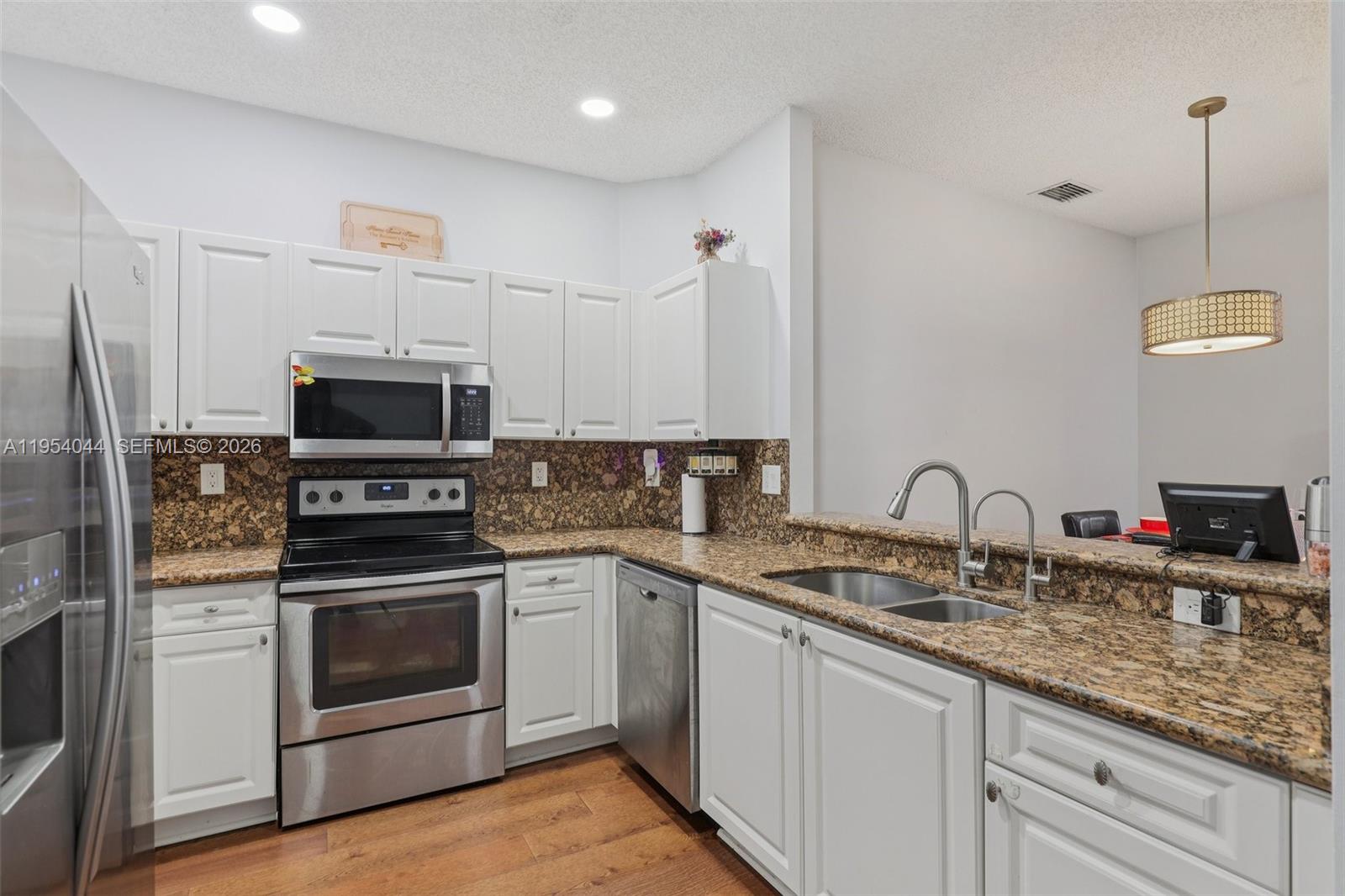 A kitchen features white cabinets, granite countertops, stainless steel appliances, and wood-look flooring — 2923 Crestwood Ter # 5104, Margate FL 33063, MARGATE, FL