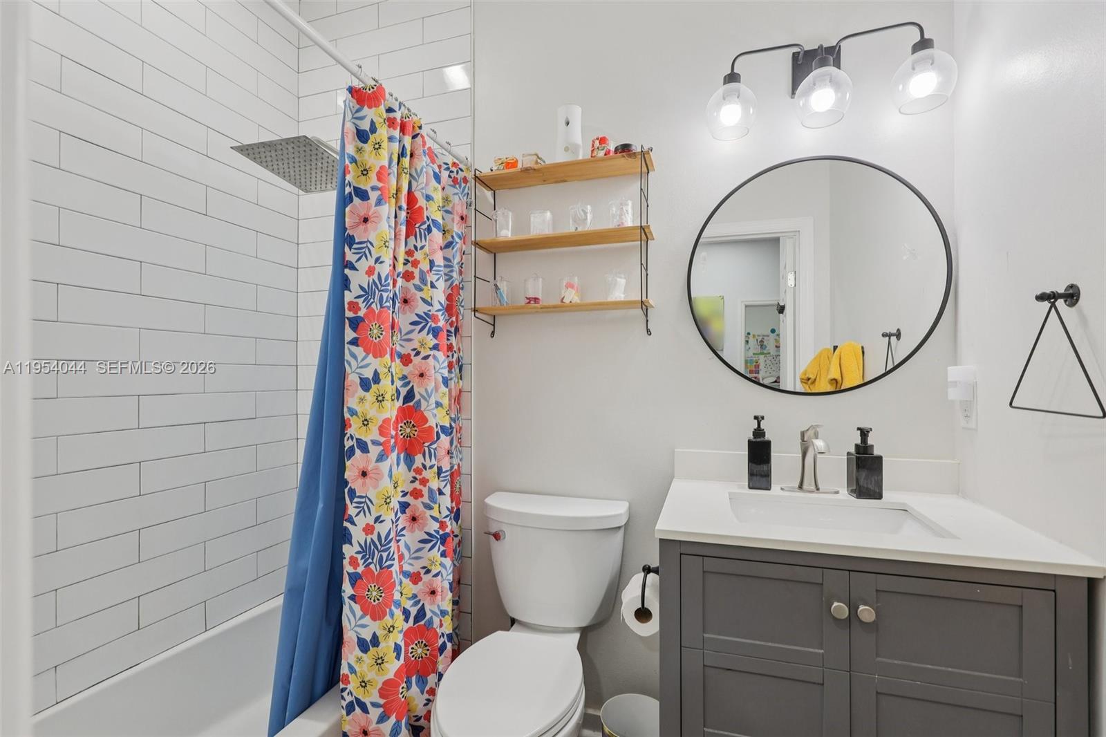 A bathroom features a gray vanity, a round mirror, a toilet, and a floral shower curtain — 2923 Crestwood Ter # 5104, Margate FL 33063, MARGATE, FL