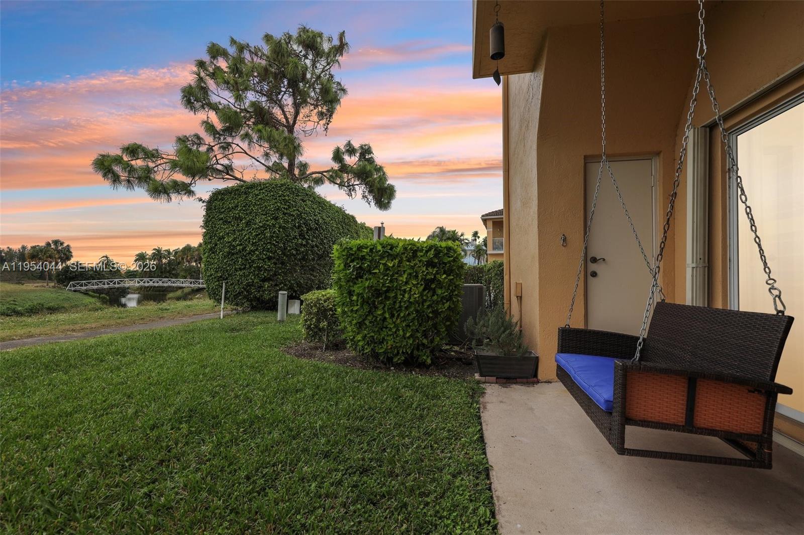 A patio with a hanging swing chair overlooks a grassy lawn and a distant bridge — 2923 Crestwood Ter # 5104, Margate FL 33063, MARGATE, FL