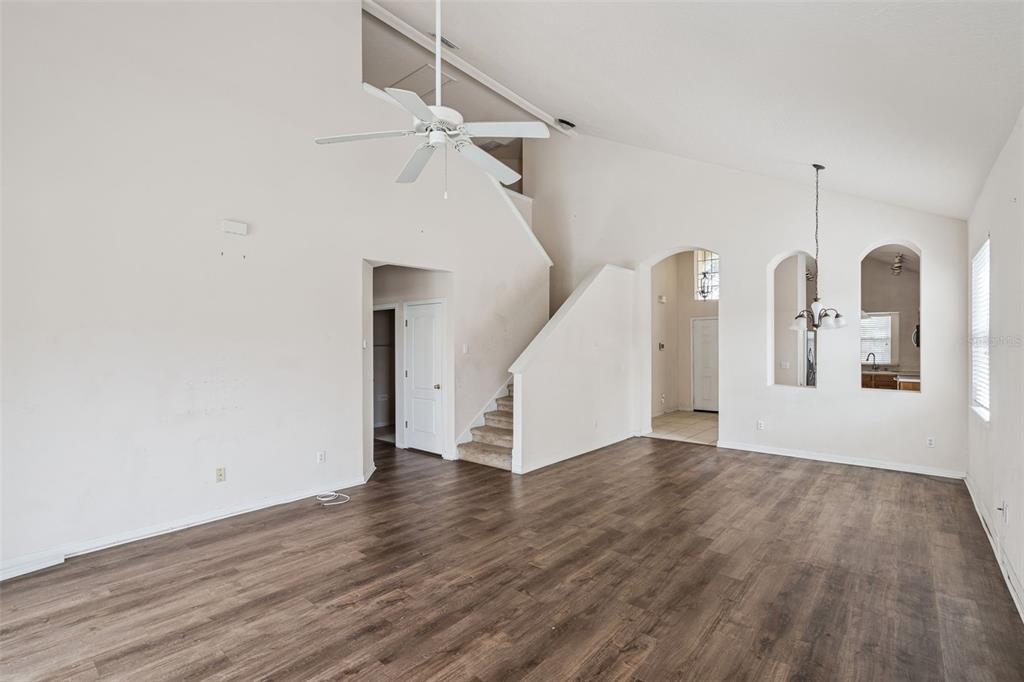A spacious living room features vaulted ceilings, wood-look flooring, a ceiling fan, and carpeted stairs — 1755 ROYAL RIDGE DRIVE, DAVENPORT, FL