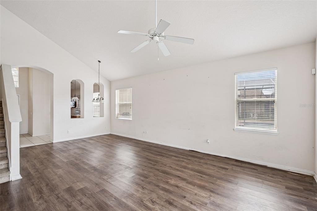 An empty living room with wood-look flooring, a vaulted ceiling, and a white ceiling fan — 1755 ROYAL RIDGE DRIVE, DAVENPORT, FL
