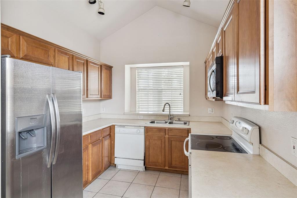 A kitchen with wood cabinets, stainless steel refrigerator, white dishwasher, and beige countertops — 1755 ROYAL RIDGE DRIVE, DAVENPORT, FL