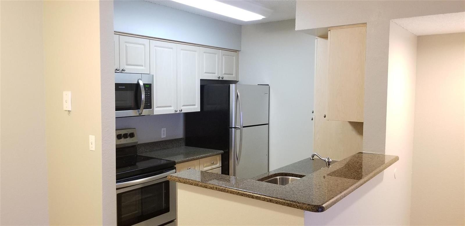A kitchen features white cabinets, stainless steel appliances, and a granite-topped breakfast bar — 2846 S University Drive # 4205, Davie FL 33328, DAVIE, FL
