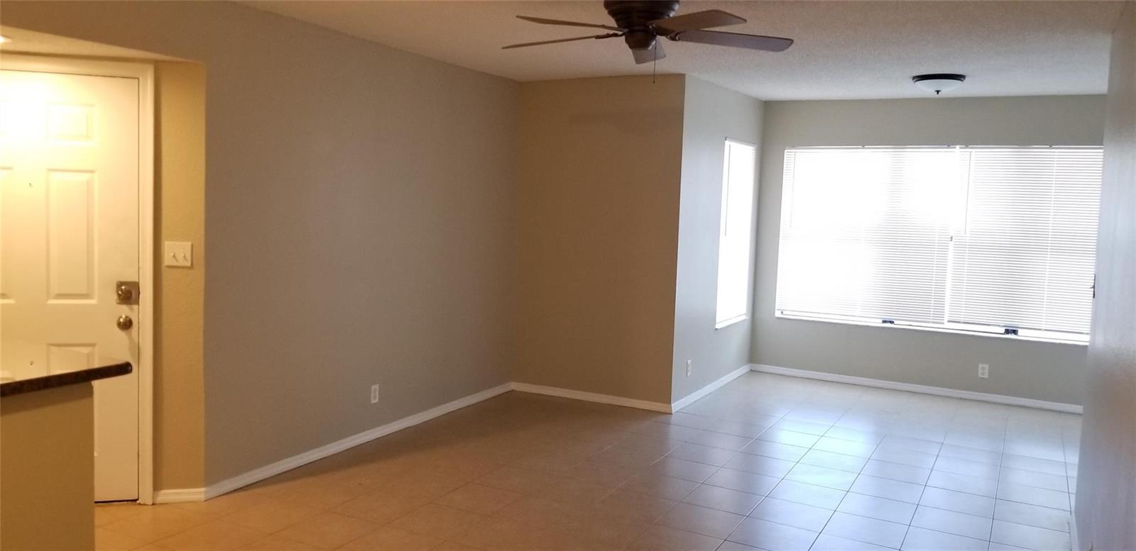 An empty living room features beige walls, tile flooring, a ceiling fan, and large windows — 2846 S University Drive # 4205, Davie FL 33328, DAVIE, FL