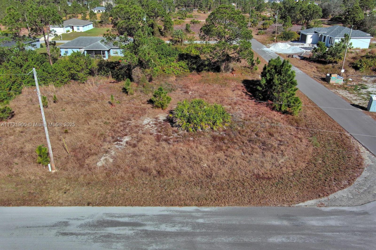 An aerial view shows a vacant, grassy residential lot situated between paved roads and houses — 733 Bumby St E, Lehigh Acres FL 33974, LEHIGH ACRES, FL
