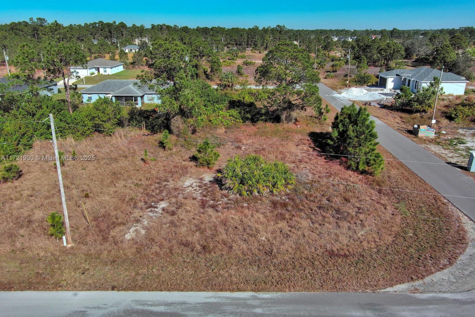 An elevated view shows a vacant, grassy residential lot bordered by paved roads and houses — 733 Bumby St E, Lehigh Acres FL 33974, LEHIGH ACRES, FL